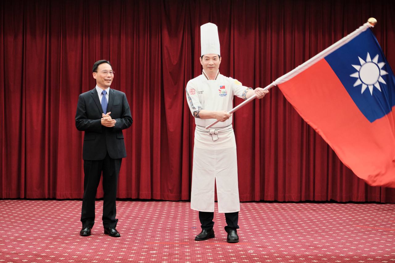 外交部亞太司司長藍夏禮，授旗給台北市烹飪商業同業公會副理事長黃景龍。